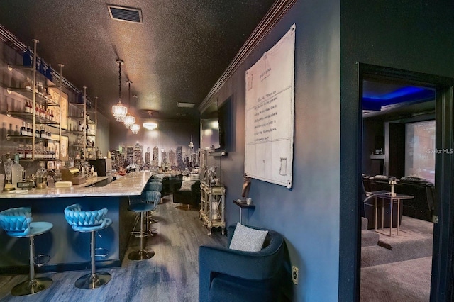 bar with a community bar, visible vents, wood finished floors, crown molding, and a textured ceiling