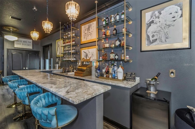 bar featuring a textured wall, wood finished floors, visible vents, fridge, and wet bar