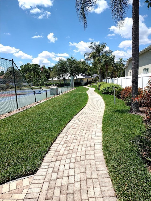 view of property's community with a tennis court, fence, and a yard