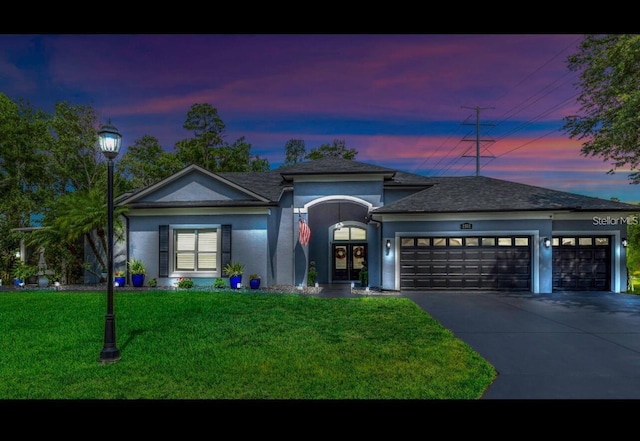 view of front of home with a garage, concrete driveway, french doors, a yard, and stucco siding