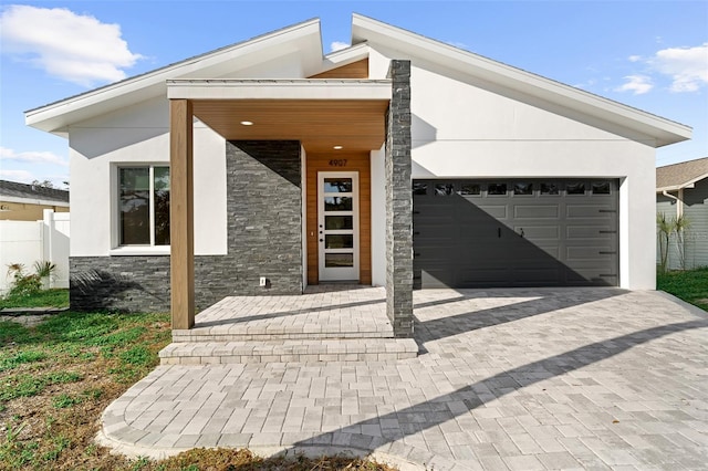 contemporary house featuring decorative driveway, stone siding, fence, and stucco siding