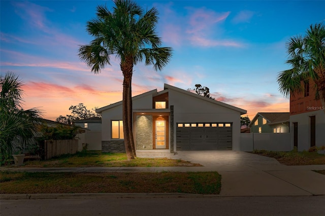 mid-century home featuring a garage, concrete driveway, fence, and stucco siding