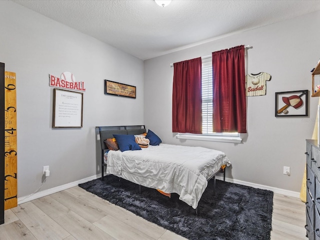 bedroom with baseboards, a textured ceiling, and light wood-style floors