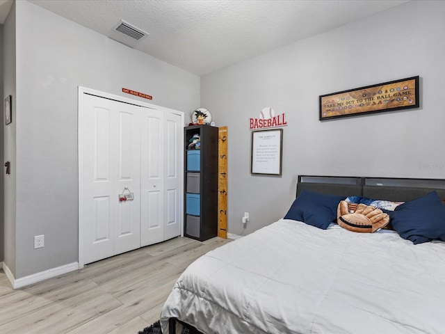 bedroom with light wood finished floors, a closet, visible vents, a textured ceiling, and baseboards