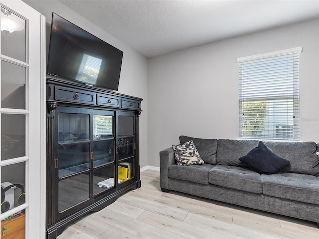 living area with light wood-style floors, a textured ceiling, and baseboards