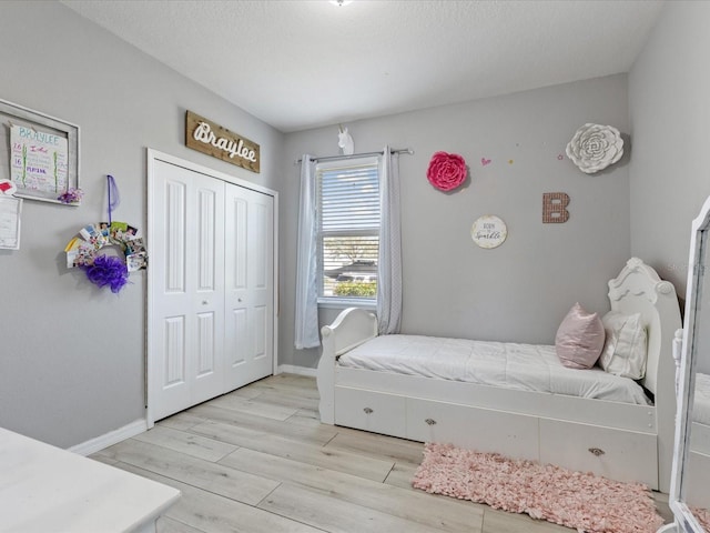 bedroom featuring light wood finished floors, a textured ceiling, baseboards, and a closet