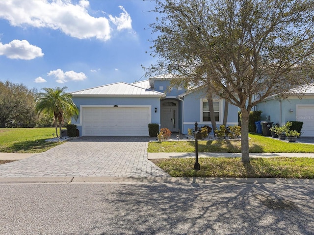 single story home featuring decorative driveway, stucco siding, an attached garage, metal roof, and a front lawn