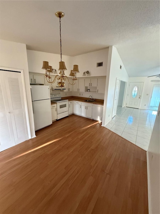 kitchen featuring visible vents, vaulted ceiling, an inviting chandelier, white appliances, and a sink