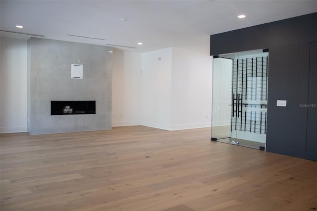 unfurnished living room with light wood finished floors, recessed lighting, baseboards, and a tile fireplace