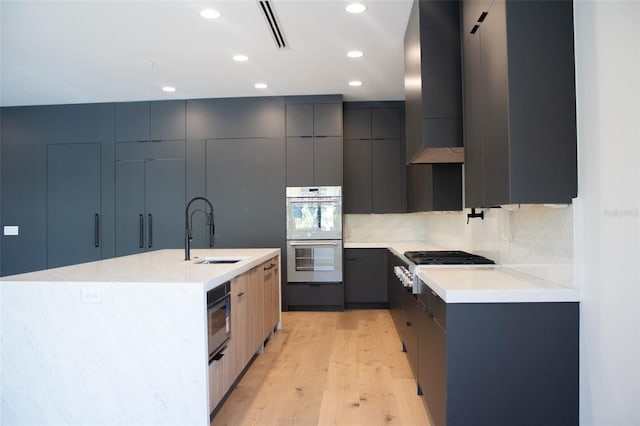 kitchen featuring stainless steel appliances, a sink, wall chimney exhaust hood, and modern cabinets