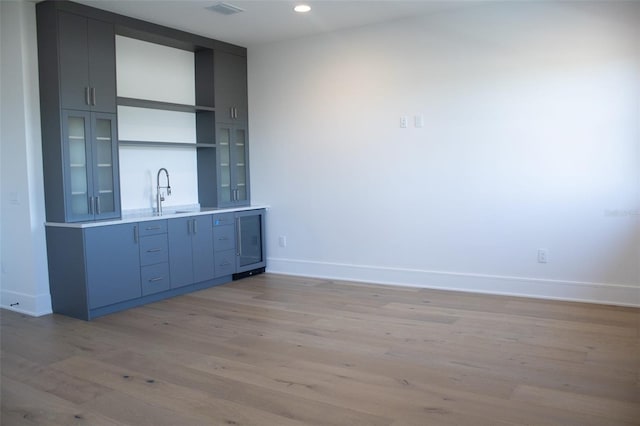 bar with wine cooler, visible vents, light wood-style floors, a sink, and baseboards