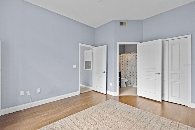 unfurnished bedroom featuring visible vents, ensuite bath, baseboards, and wood finished floors