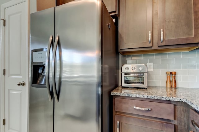 kitchen with stainless steel refrigerator with ice dispenser, backsplash, and light stone countertops