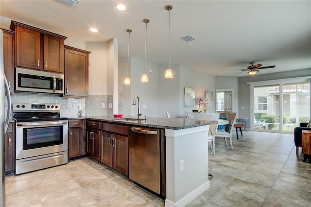 kitchen with dark stone counters, decorative backsplash, a peninsula, stainless steel appliances, and a sink