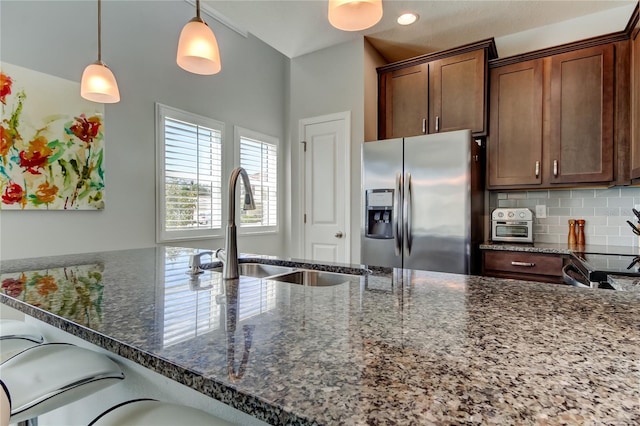 kitchen featuring dark stone counters, a sink, stainless steel refrigerator with ice dispenser, and decorative backsplash