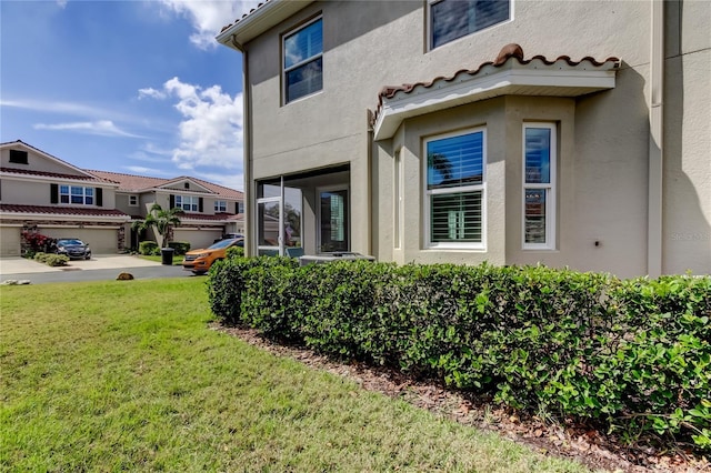 view of property exterior featuring a yard, a tiled roof, and stucco siding