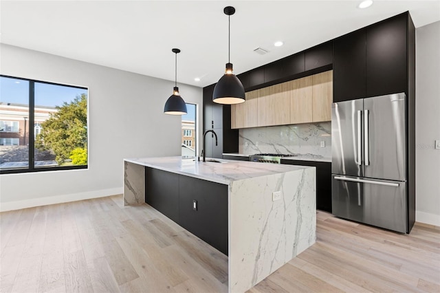 kitchen featuring decorative backsplash, modern cabinets, stainless steel refrigerator, dark cabinetry, and a sink