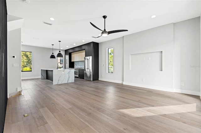 unfurnished living room with light wood-type flooring, a sink, a ceiling fan, and baseboards