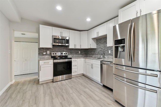 kitchen with decorative backsplash, light stone counters, stainless steel appliances, white cabinetry, and a sink