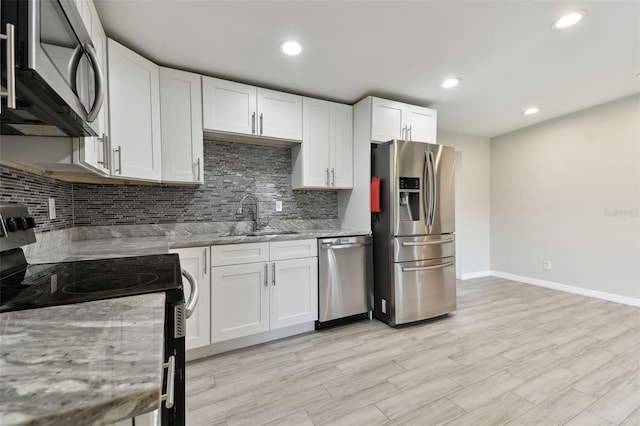 kitchen with light stone counters, backsplash, appliances with stainless steel finishes, white cabinetry, and a sink