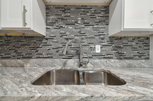 kitchen featuring light stone counters, white cabinetry, a sink, and backsplash