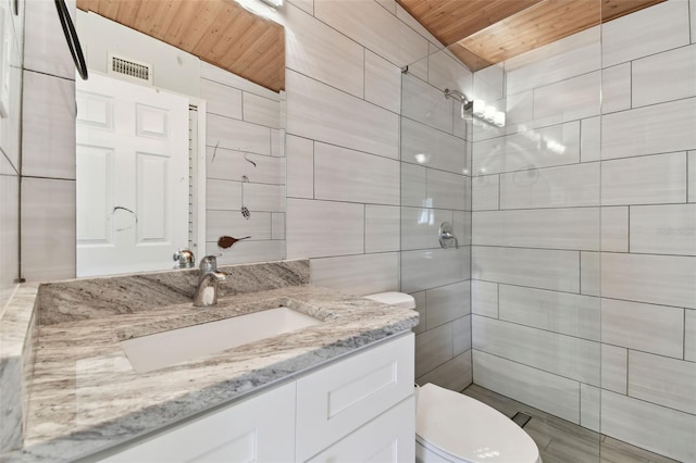 full bath featuring visible vents, a tile shower, tile walls, and vanity