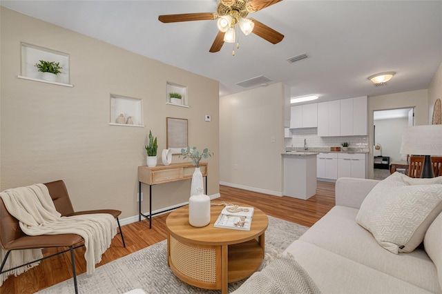 living room with baseboards, ceiling fan, visible vents, and light wood-style floors