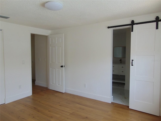 unfurnished bedroom featuring light wood-style floors, a barn door, visible vents, and baseboards