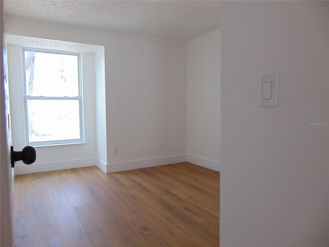 unfurnished room with light wood-style floors, a textured ceiling, and baseboards