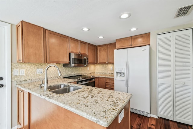 kitchen featuring brown cabinetry, visible vents, a peninsula, a sink, and stainless steel appliances