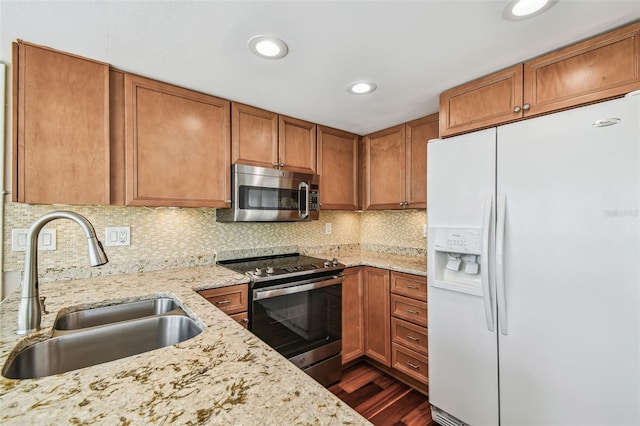 kitchen with a sink, light stone counters, dark wood finished floors, stainless steel appliances, and brown cabinetry