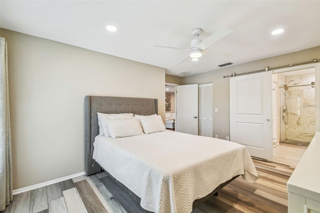 bedroom with visible vents, baseboards, a barn door, ensuite bathroom, and wood finished floors