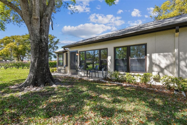 rear view of property featuring a yard, a patio, and stucco siding