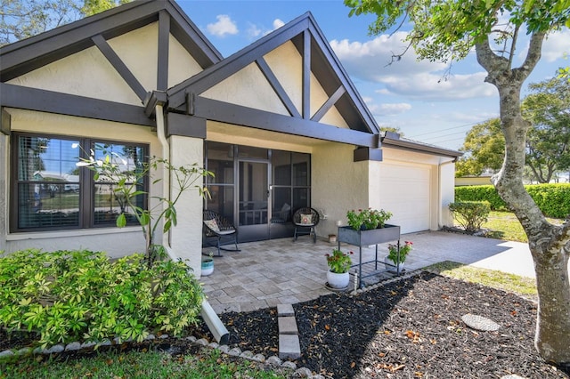 rear view of house featuring an attached garage, driveway, a sunroom, and stucco siding