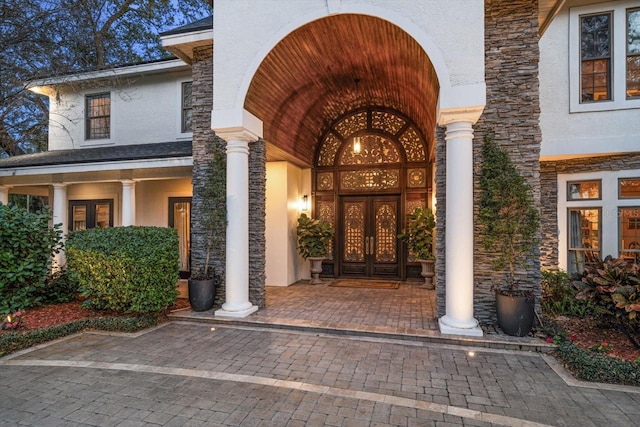 doorway to property with stucco siding, stone siding, and french doors