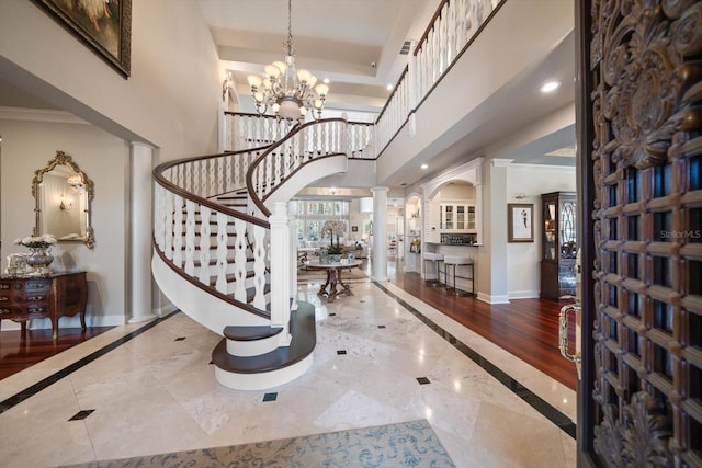 entrance foyer featuring a tray ceiling, a notable chandelier, ornate columns, baseboards, and stairs