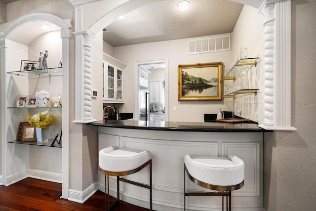 bar featuring decorative columns, visible vents, baseboards, dark wood-style floors, and wet bar