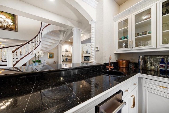 kitchen with tile counters, white cabinets, glass insert cabinets, ornate columns, and a sink