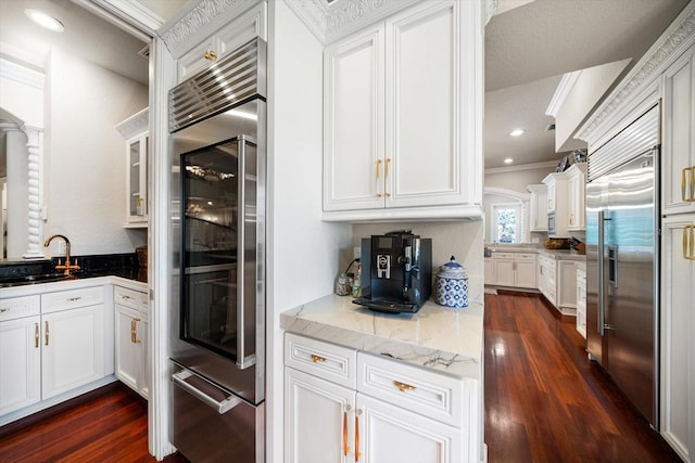 kitchen with dark wood-type flooring, a sink, white cabinets, ornamental molding, and stainless steel built in refrigerator