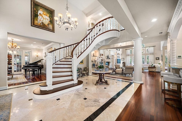 foyer with a fireplace, ornate columns, an inviting chandelier, baseboards, and stairs