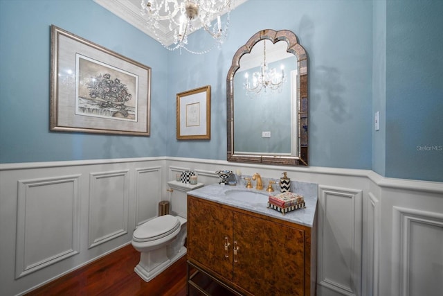 half bathroom featuring wainscoting, a notable chandelier, vanity, and toilet