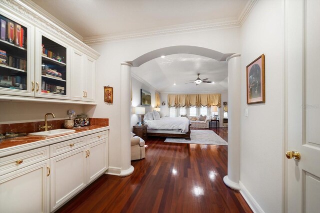 bedroom with arched walkways, dark wood-style flooring, crown molding, a sink, and baseboards