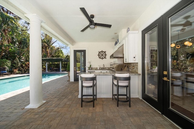 view of patio / terrace with outdoor wet bar, area for grilling, a sink, a ceiling fan, and an outdoor pool