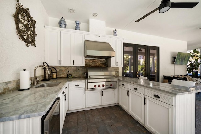 kitchen featuring a peninsula, wall chimney exhaust hood, white cabinetry, and a sink