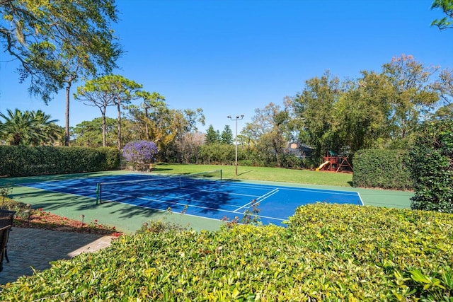 view of tennis court with a lawn and playground community