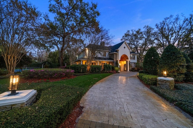 view of front facade with decorative driveway, a front yard, stone siding, and a chimney