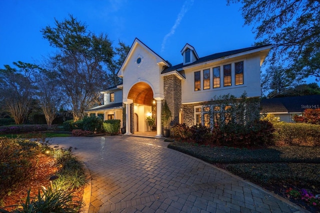 view of front of house featuring stone siding, decorative driveway, and stucco siding