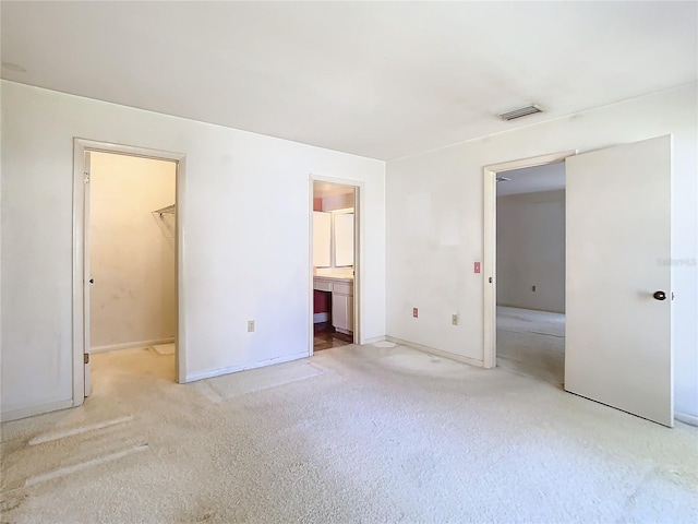 unfurnished bedroom with ensuite bathroom, carpet flooring, visible vents, baseboards, and a walk in closet