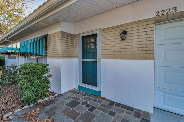 entrance to property featuring a garage and brick siding