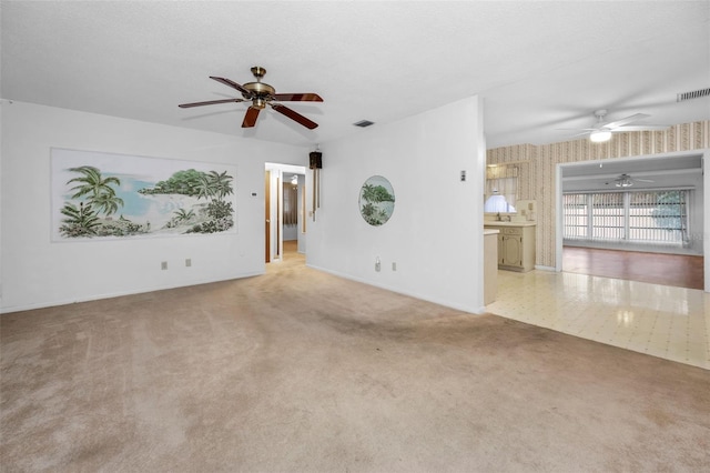 unfurnished living room featuring a textured ceiling, carpet, visible vents, and wallpapered walls